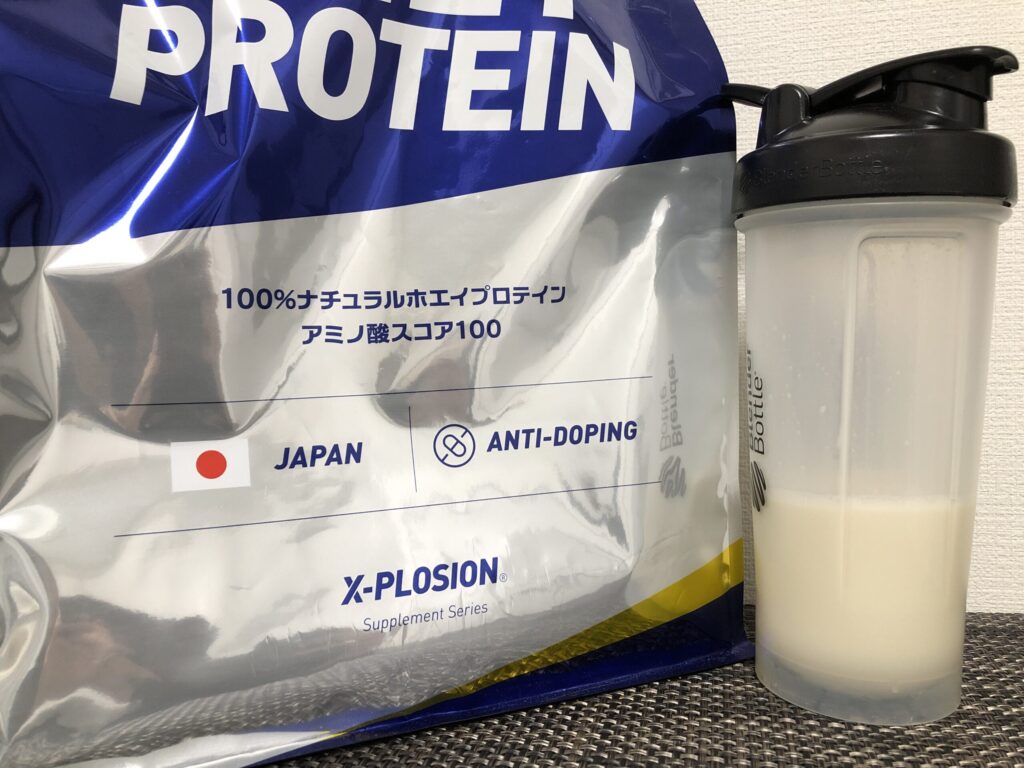 エクスプロージョンのバニラ味のパッケージと、シェイカーで溶かしたプロテインが並べて置かれている画像