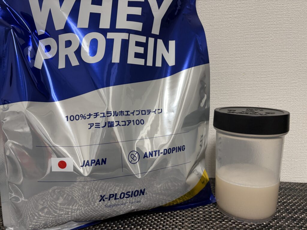 エクスプロージョンのおしるこ味のパッケージと、シェイカーで溶かしたプロテインが並べて置かれている画像